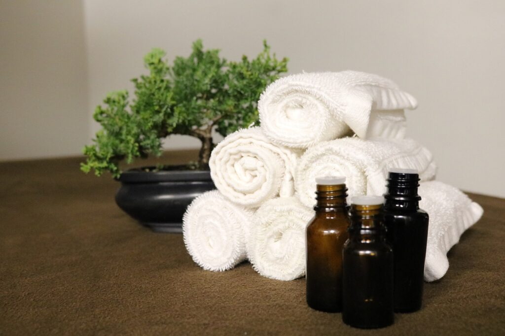 Huiles pour massage relaxant énergétique posées sur une table en bois à coté de serviettes enroulées et un bonsaï